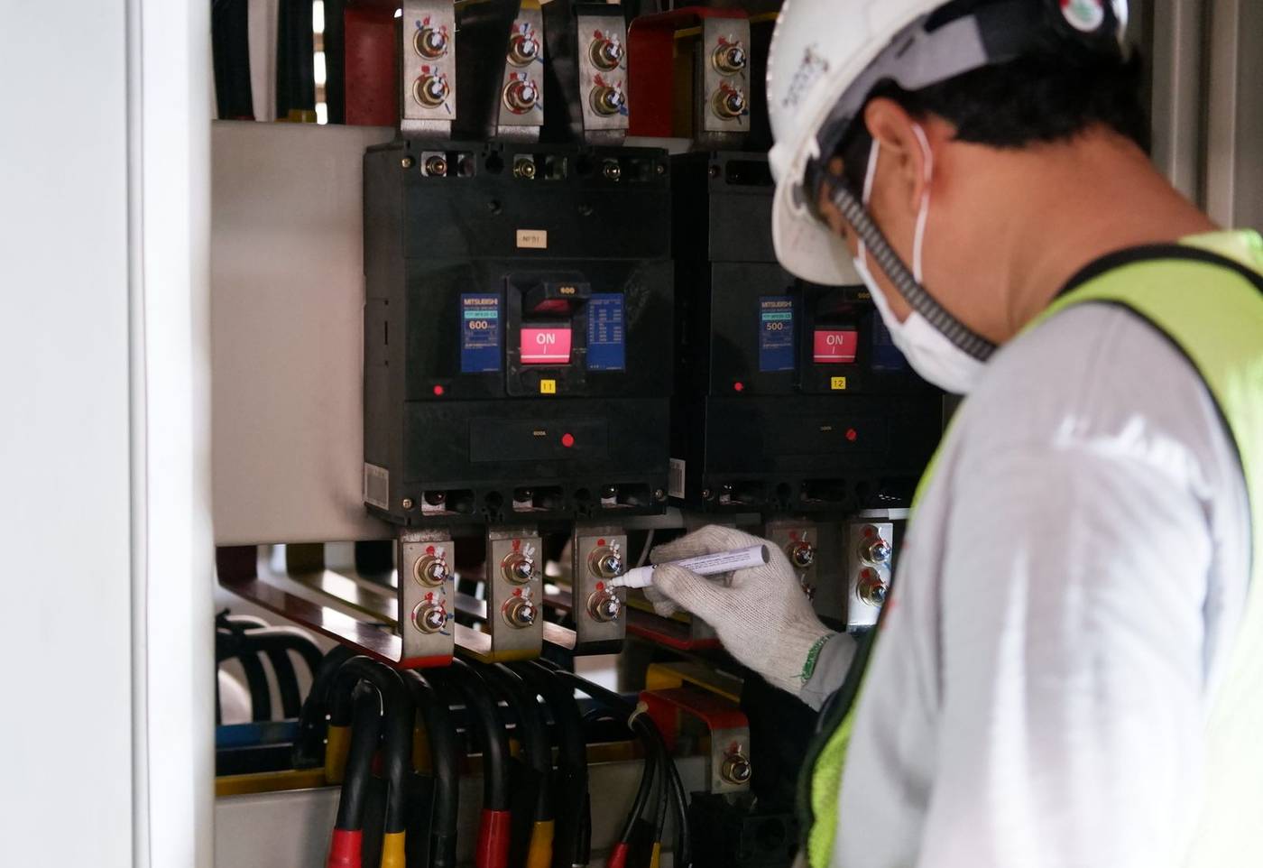 Technik v ochrannej prilbe kontroluje istič v priemyselnom rozvádzači